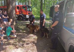 Policjanci stoją z psami na przeciwko grupy dzieci